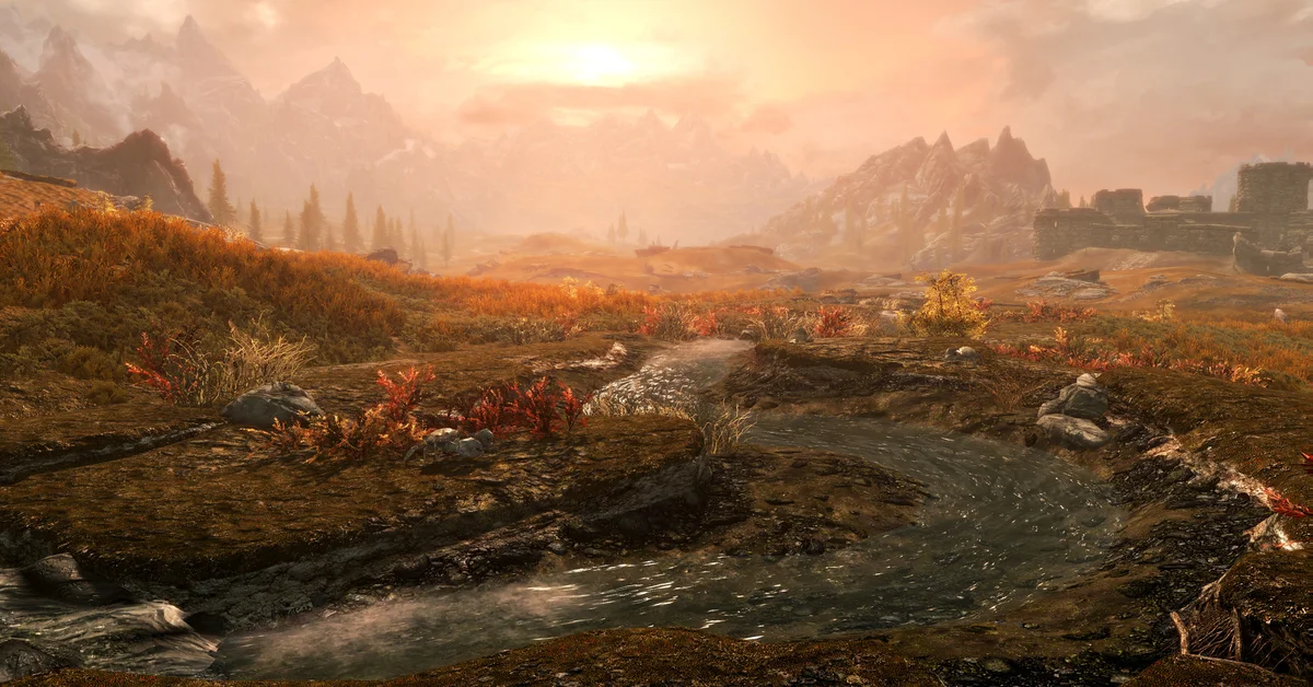 A shallow stream winding through golden autumn tundra toward misty mountains and a ruined stone fort at sunset in Skyrim