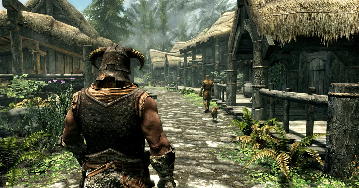 A player in a horned iron helmet walks down a stone path between thatched-roof wooden houses in a Skyrim village