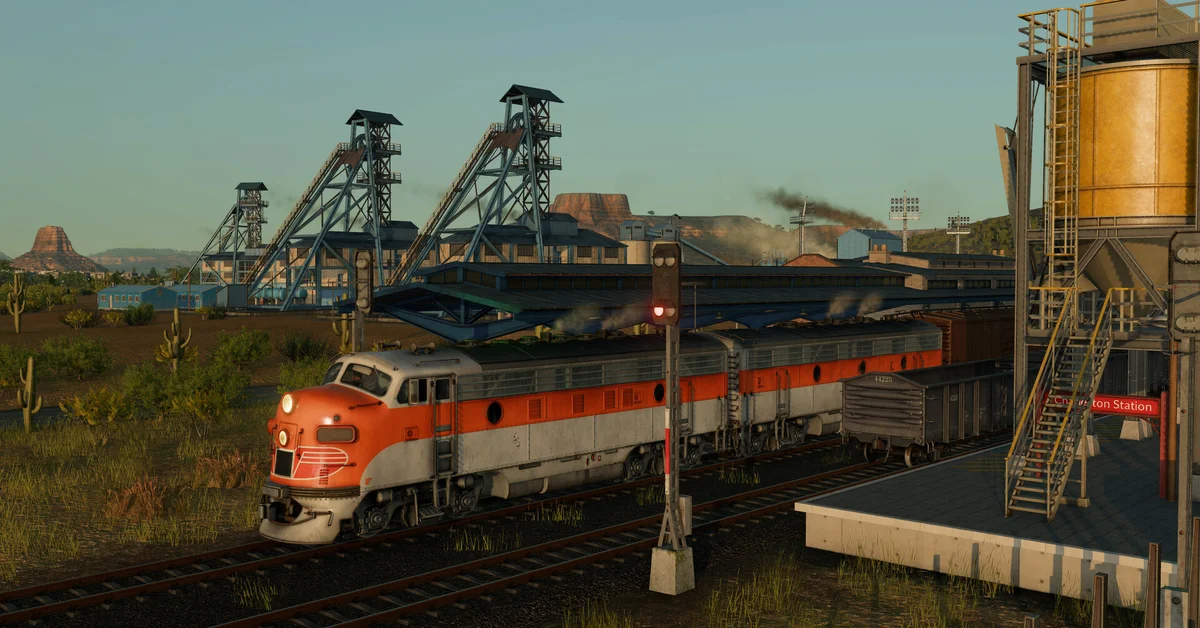 An orange and silver diesel locomotive beside a mine and silo in desert country in Transport Fever 3