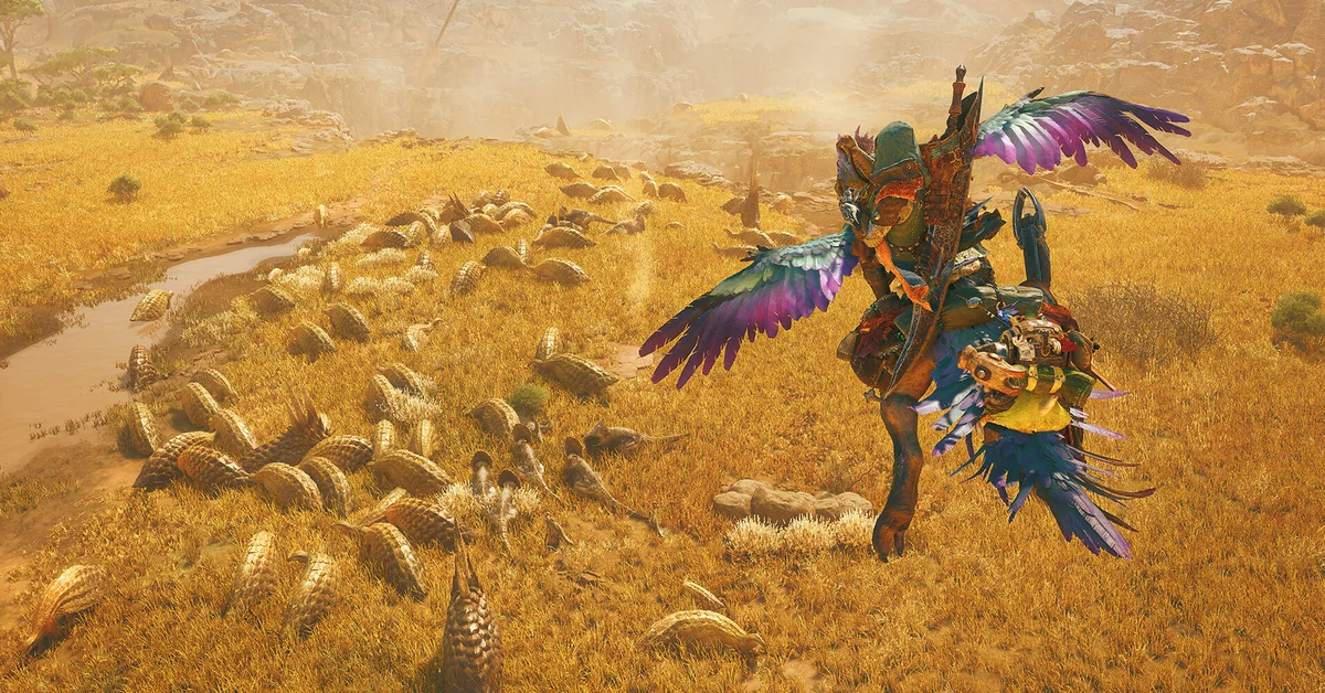 A hunter rides a feathered Seikret across the golden grass of the Windward Plains past a herd of armored monsters in Monster Hunter Wilds